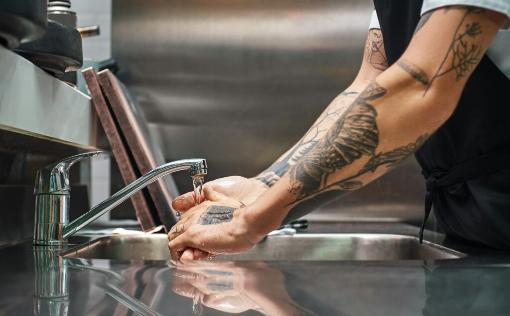 Close up photo of chef carefully washing his hands with different tattoos in a restaurant kitchen.